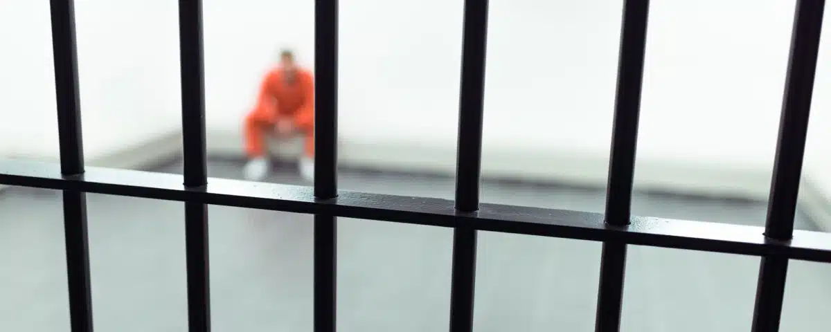 prisoner sitting on bench with prison bars on foreground